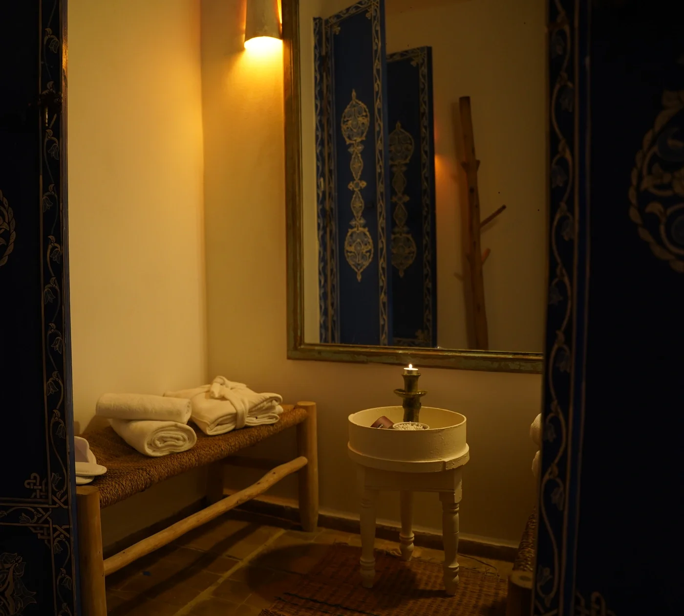 Reflejo en el espejo de las puertas azules talladas, con albornoces doblados y una vela encendida