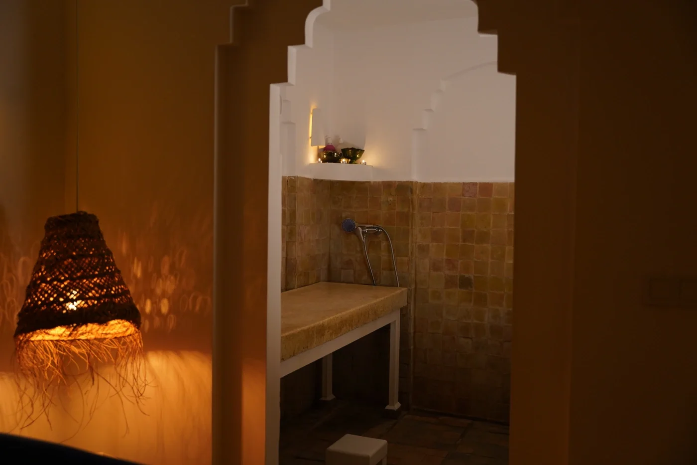 Lámpara de mimbre encendida junto a la entrada a una camilla de hammam con azulejos